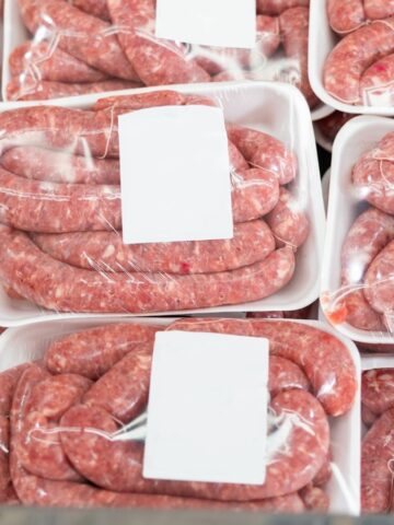 Plastic-wrapped packages of raw sausages with blank white labels stacked on a display.