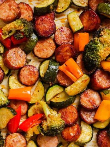 Sliced sausage, zucchini, broccoli, and bell peppers roasted on a sheet pan.