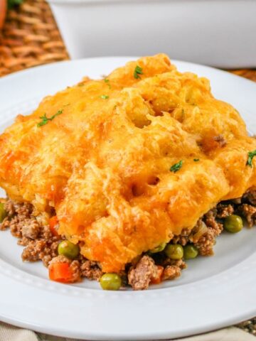 Shepherd’s pie with golden mashed potato topping, ground meat, peas, and carrots on a white plate.