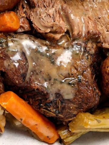 Plate of pot roast with gravy, carrots, celery, potatoes, and a baked potato with cheese on the side.