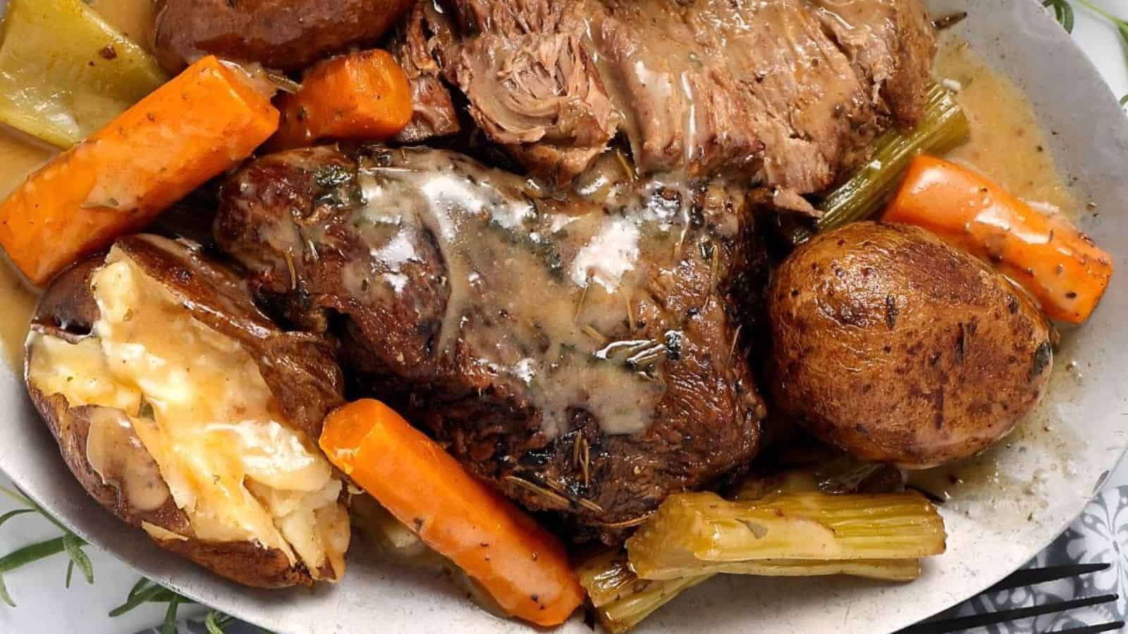 Plate of pot roast with gravy, carrots, celery, potatoes, and a baked potato with cheese on the side.