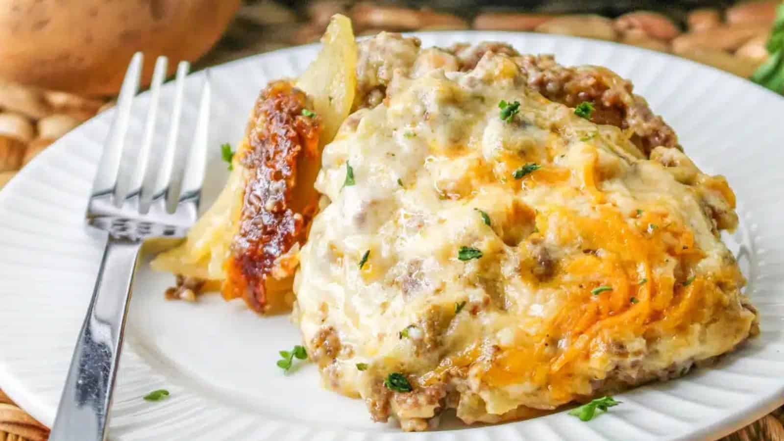 A plate of cheesy beef and potato casserole garnished with herbs, served with a fork. A potato, greenery, and a slow cooker are visible in the background.
