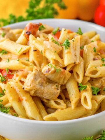 Bowl of creamy penne pasta with chicken, red peppers, and herbs, garnished with parsley.