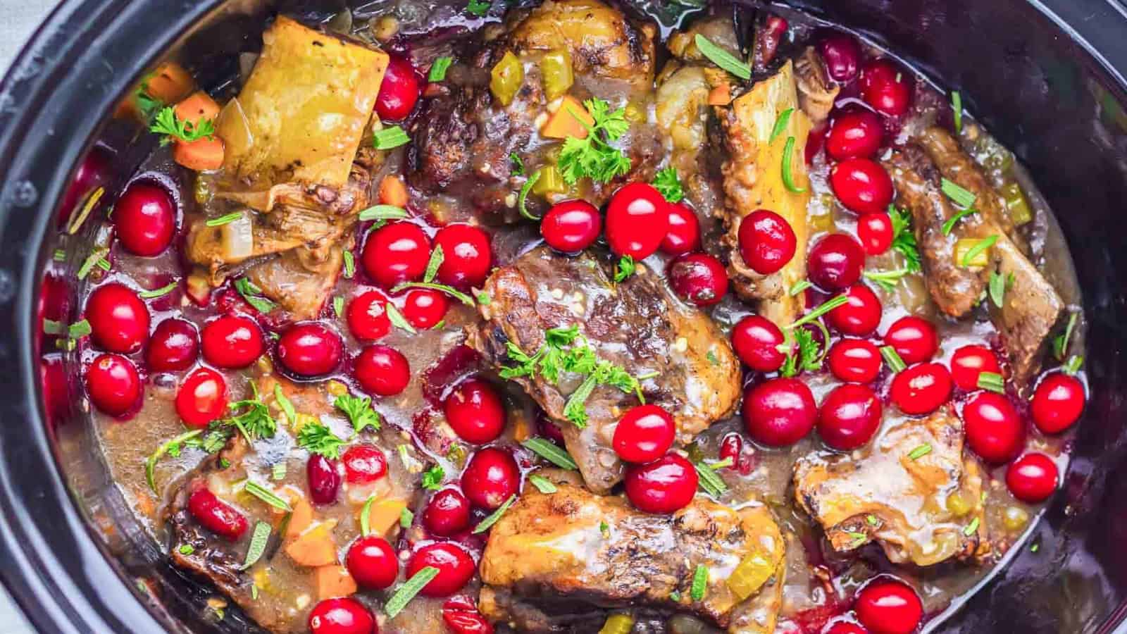 Slow-cooked beef stew with red cranberries, vegetables, and fresh herbs in a black crockpot.
