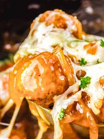Spoonful of cheesy meatballs topped with melted cheese and parsley, covered in brown gravy.
