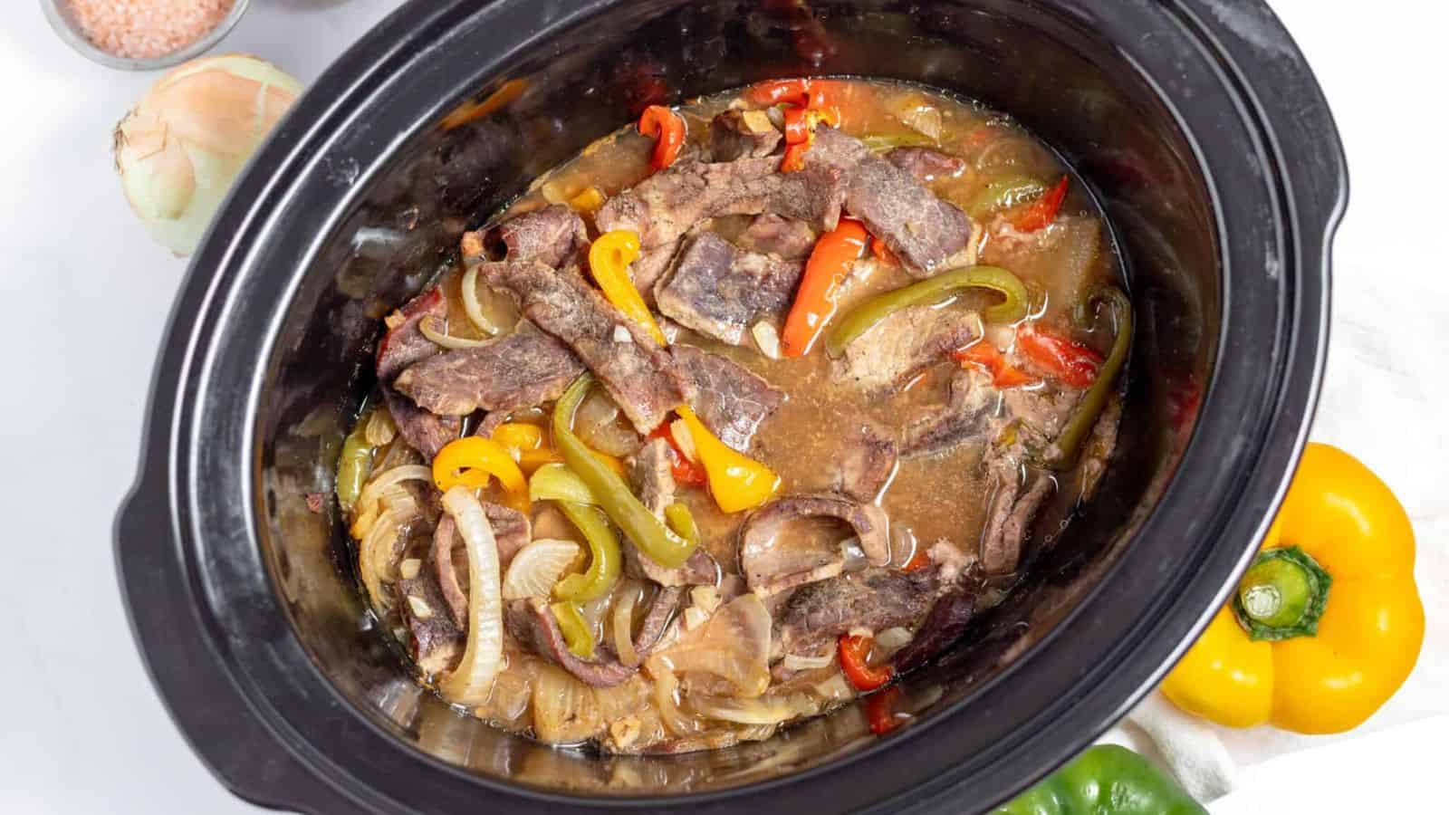 A crock pot filled with beef and peppers.