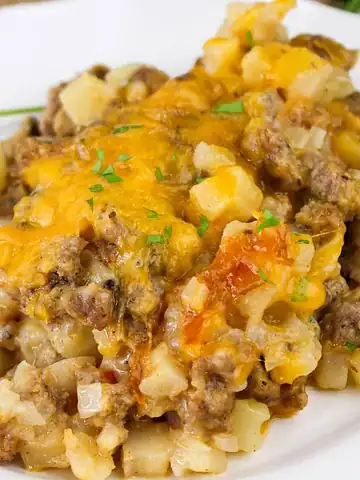 A serving of cheesy hashbrown casserole with ground beef on a white plate, garnished with parsley.