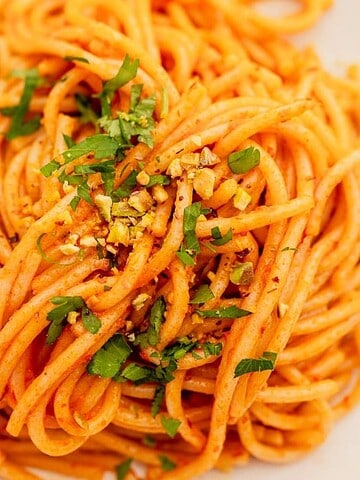 A plate of spaghetti with tomato sauce, garnished with chopped herbs, next to a fork.