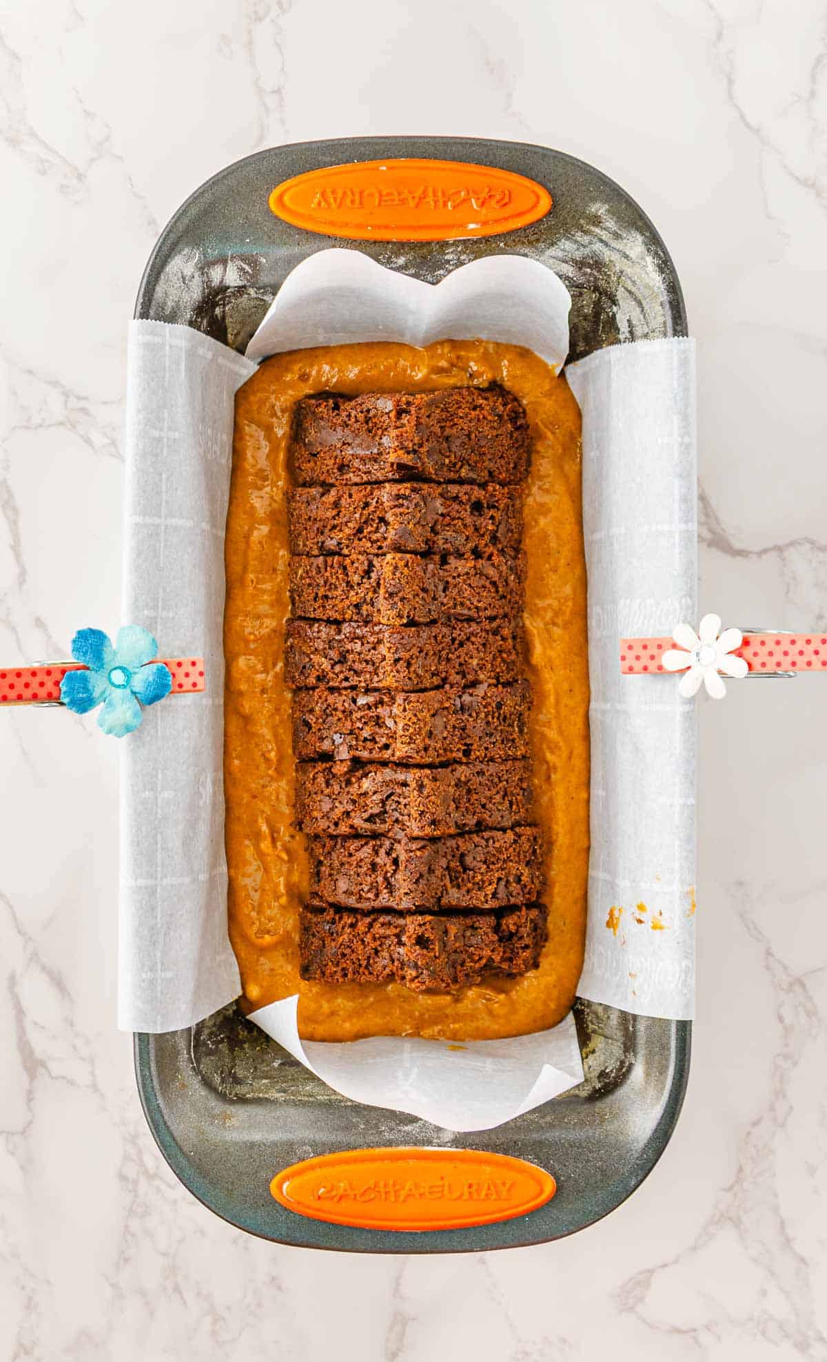 A loaf pan with Pumpkin Banana Bread batter and sliced chocolate cake in the center, lined with parchment paper&mdash;perfect for a festive Halloween Surprise.