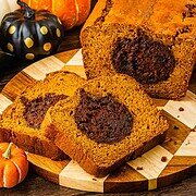 Sliced Pumpkin Banana Bread with a chocolate swirl, displayed on a wooden board alongside decorative pumpkins—perfect for your Halloween table.