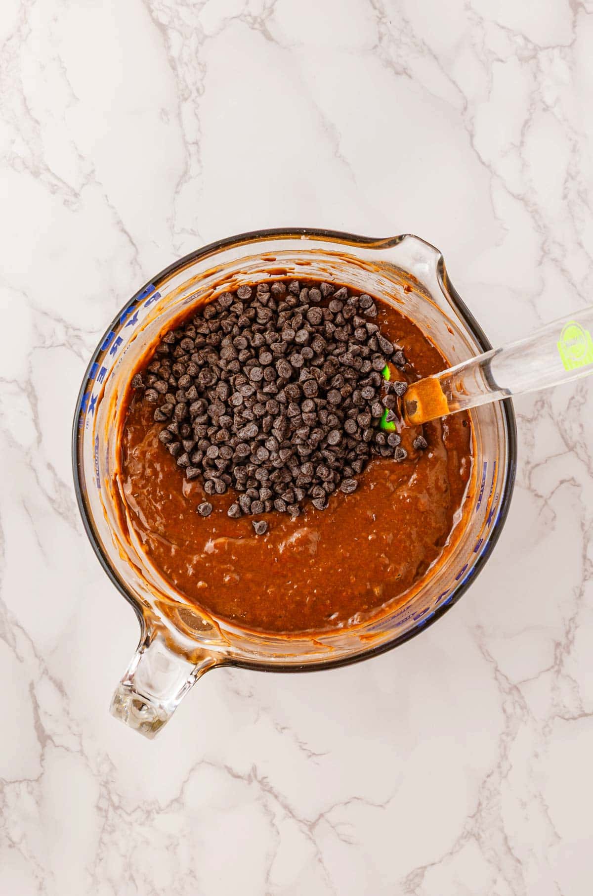 Glass bowl with chocolate brownie batter and chocolate chips, being mixed with a spatula on a marble surface&mdash;perfect for whipping up Halloween treats or pairing alongside cozy Pumpkin Banana Bread.