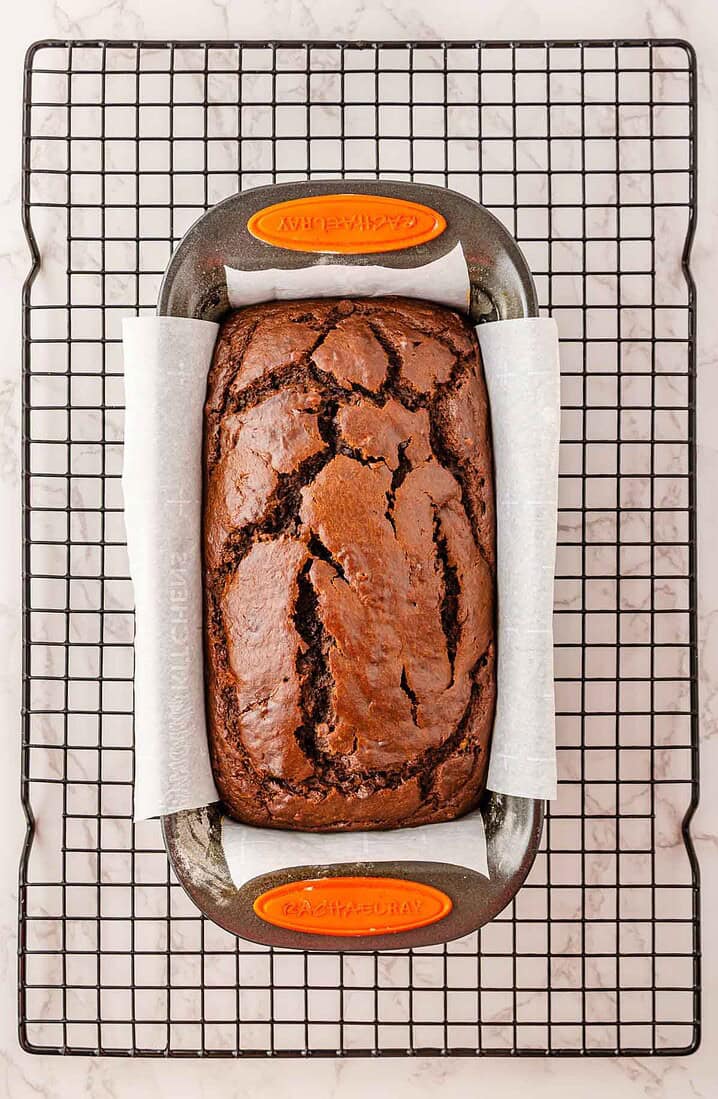 A loaf of chocolate bread in a lined pan, cooling on a wire rack&mdash;perfect for a cozy Halloween treat or to enjoy alongside your favorite Pumpkin Banana Bread.