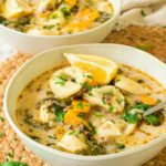 Three bowls of creamy Italian tortellini soup with potatoes, carrots, greens, and lemon wedges, garnished with chopped herbs.