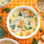 A bowl of creamy potato soup with Tuscan sausage, carrots, and kale, served on an orange tiled surface.