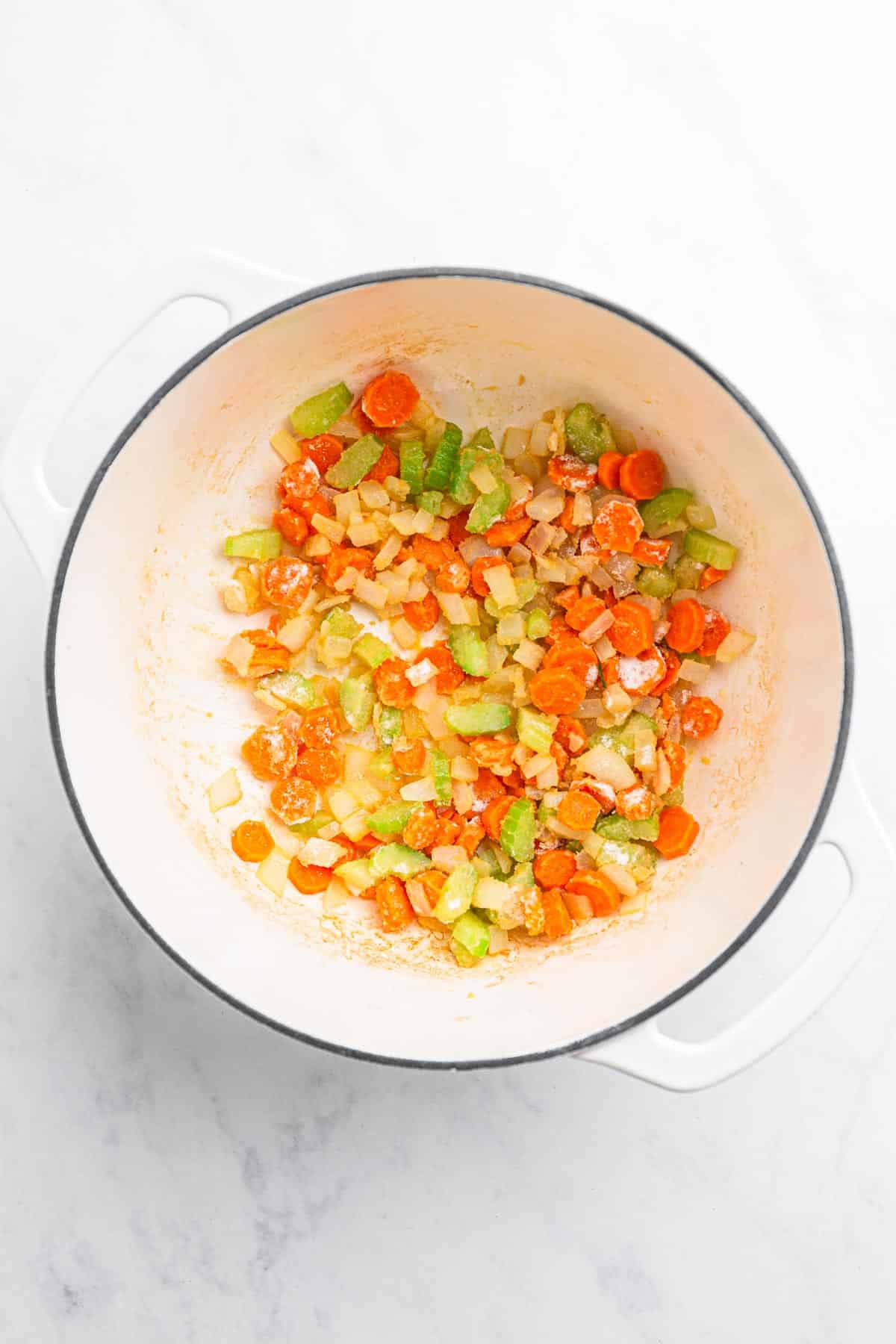 Chopped carrots, celery, and onions saut&eacute;ing in a white pot on a marble countertop&mdash;perfect beginnings for a hearty potato soup recipe.