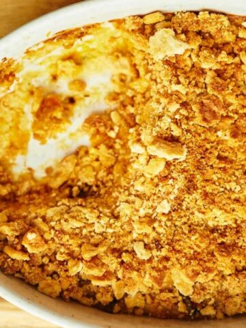 Baked casserole with a golden crumb topping in a white dish, partially scooped out.