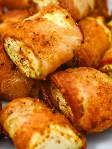 Bacon-wrapped, seasoned pieces of chicken arranged on a white plate.