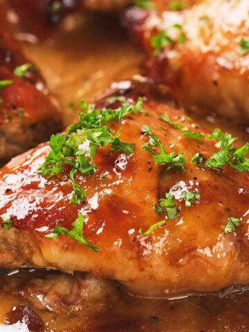Glazed baked chicken thighs in sauce, garnished with chopped parsley in a white baking dish.
