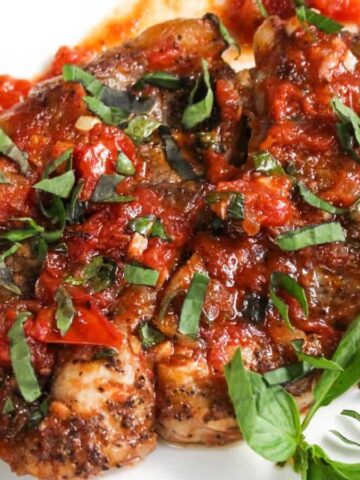 Chicken breasts topped with tomato sauce and fresh basil, served on a white plate.