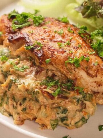 Grilled chicken breast with creamy spinach filling, garnished with parsley and served with fresh lettuce.