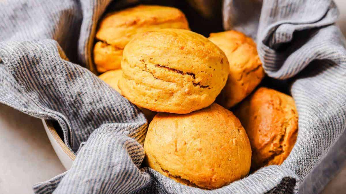 A basket lined with a gray cloth holds several golden brown, freshly baked biscuits.
