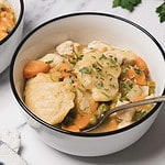 A comforting bowl of Chicken and Dumplings stew with carrots, peas, and parsley, served with a spoon—an easy skillet meal perfect for cozy nights.