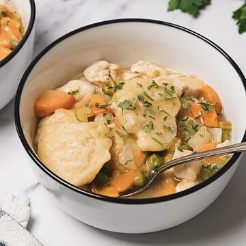 A comforting bowl of Chicken and Dumplings stew with carrots, peas, and parsley, served with a spoon—an easy skillet meal perfect for cozy nights.