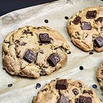 Close-up of thick Chocolate Chunk Cookies with large chocolate pieces, fresh from the Air Fryer, on a parchment-lined baking tray.
