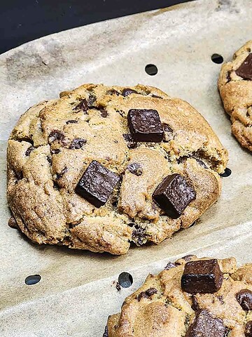 Close-up of thick Chocolate Chunk Cookies with large chocolate pieces, fresh from the Air Fryer, on a parchment-lined baking tray.
