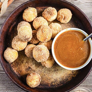 Round cinnamon sugar donut holes on a plate with a bowl of caramel dipping sauce and a spoon.