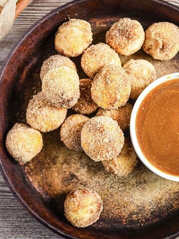 Round cinnamon sugar donut holes on a plate with a bowl of caramel dipping sauce and a spoon.