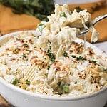 A fork holds creamy pasta bake with peas above a cheese-topped casserole dish.
