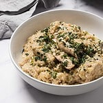 A bowl of creamy chicken and dumplings garnished with chopped herbs on a white surface.