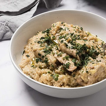A bowl of creamy chicken and dumplings garnished with chopped herbs on a white surface.