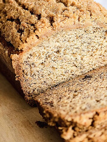 Sliced loaf of banana bread with a crumbly streusel topping on a wooden cutting board, showcasing the perfect blend of moist banana bread and sweet, crunchy streusel topping.