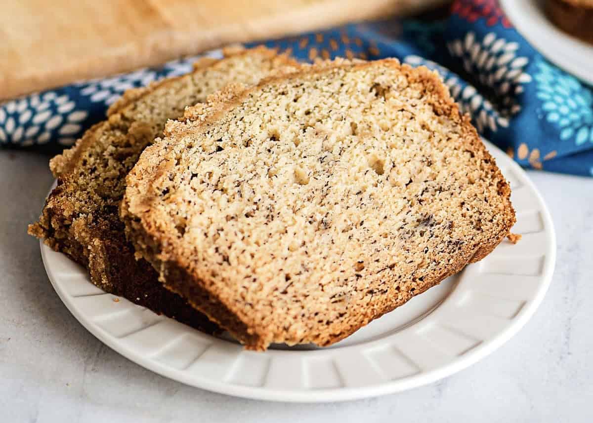 Two thick slices of banana bread with a streusel topping sit on a white plate, accented by a colorful napkin in the background.