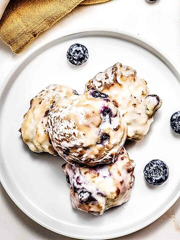 Iced blueberry cookies on a white plate with fresh blueberries and air fryer blueberry donut holes beside them, seen from above.