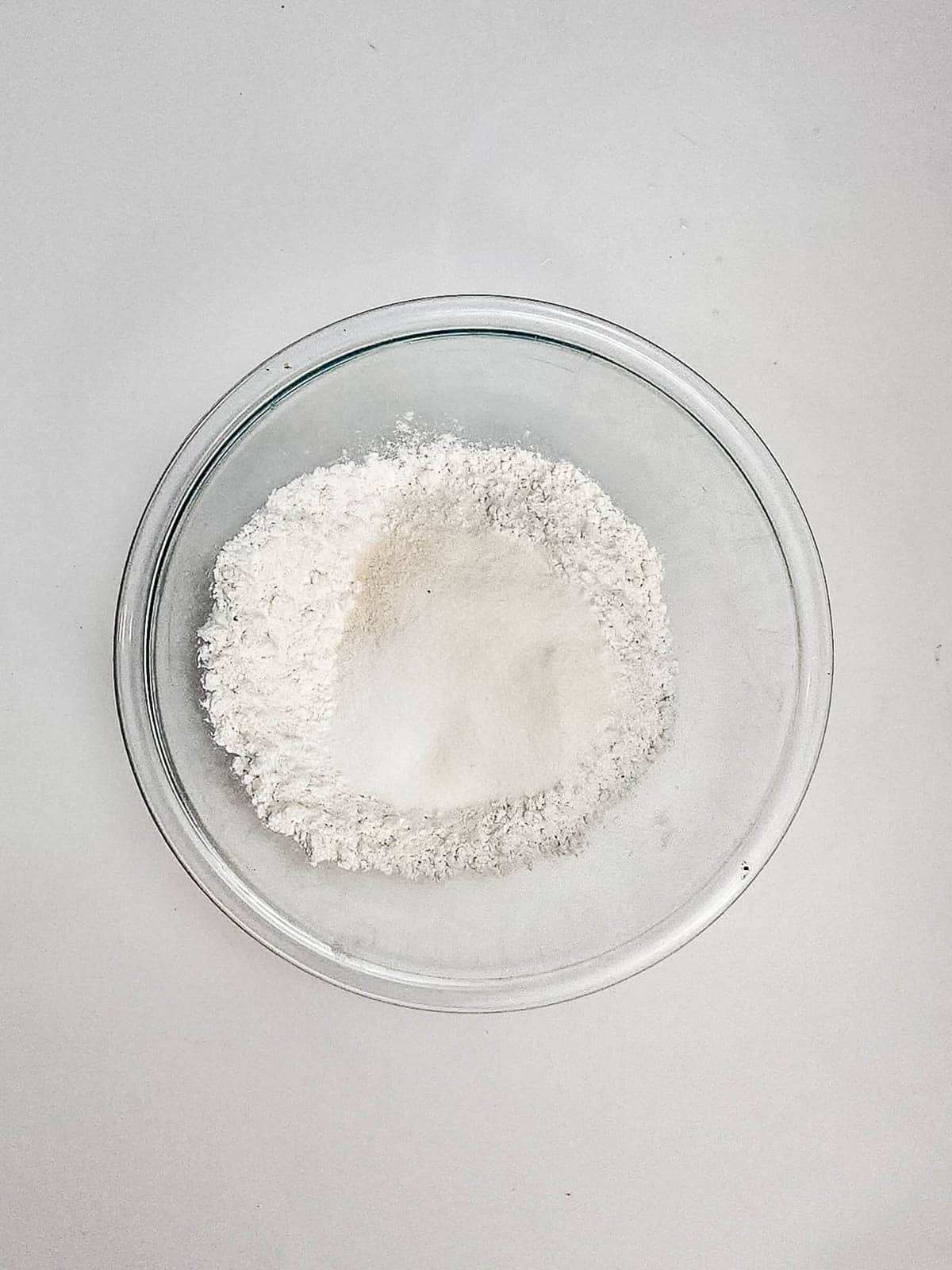 A clear glass bowl filled with white flour sits on a plain white surface, ready to help you create delicious Air Fryer Blueberry Donut Holes.