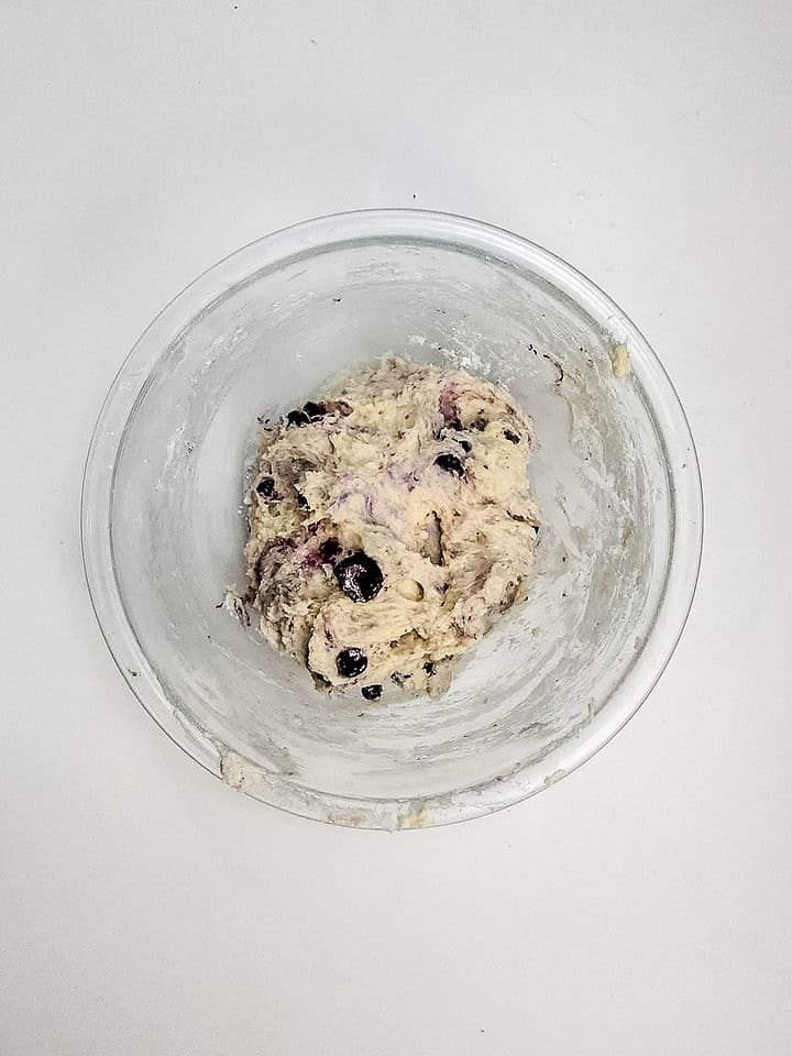 A glass bowl with blueberry scone dough, perfect for making Air Fryer Blueberry Donut Holes, sits on a white surface, viewed from above.