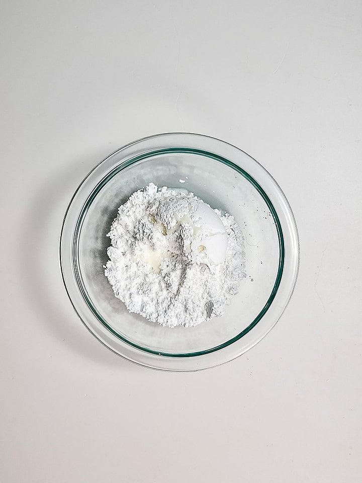 A glass bowl with powdered sugar and an egg on a white surface, perfect for making Air Fryer Blueberry Donut Holes.
