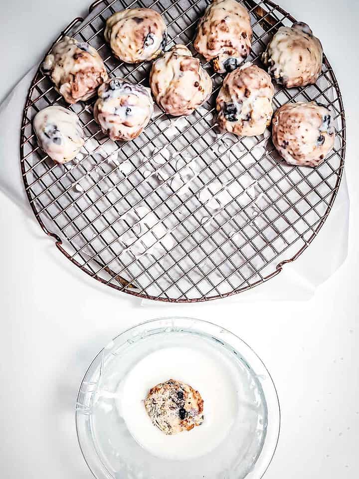 Iced scones on a wire rack, with one being dipped in glaze in a glass bowl below—just like making air fryer blueberry donut holes for the perfect sweet treat.