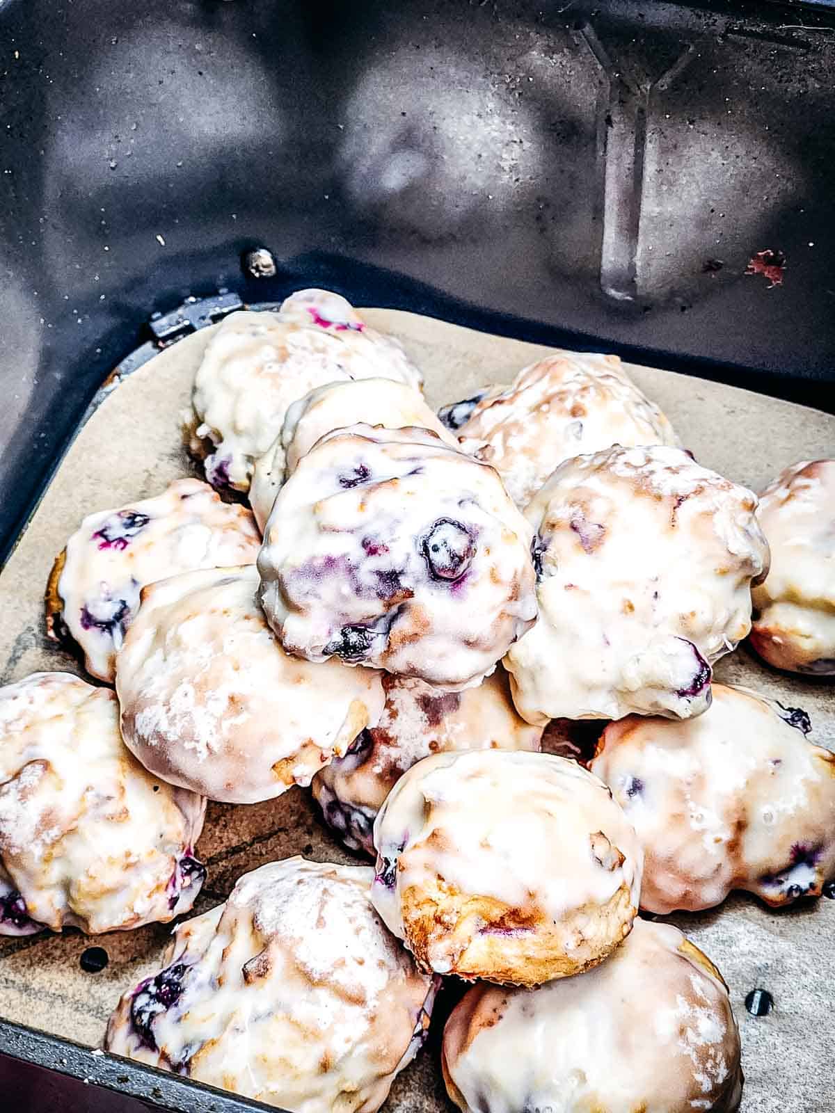 A pile of glazed blueberry donut holes on parchment paper rests inside a metal container, perfect for an easy air fryer treat.