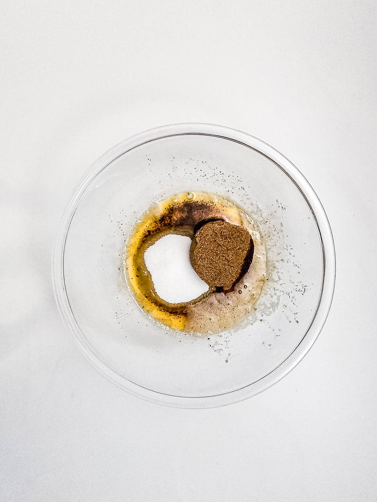 A glass bowl with brown sugar, white sugar, and wet ingredients on a white surface&mdash;perfect for mixing up delicious Air Fryer Cookies.