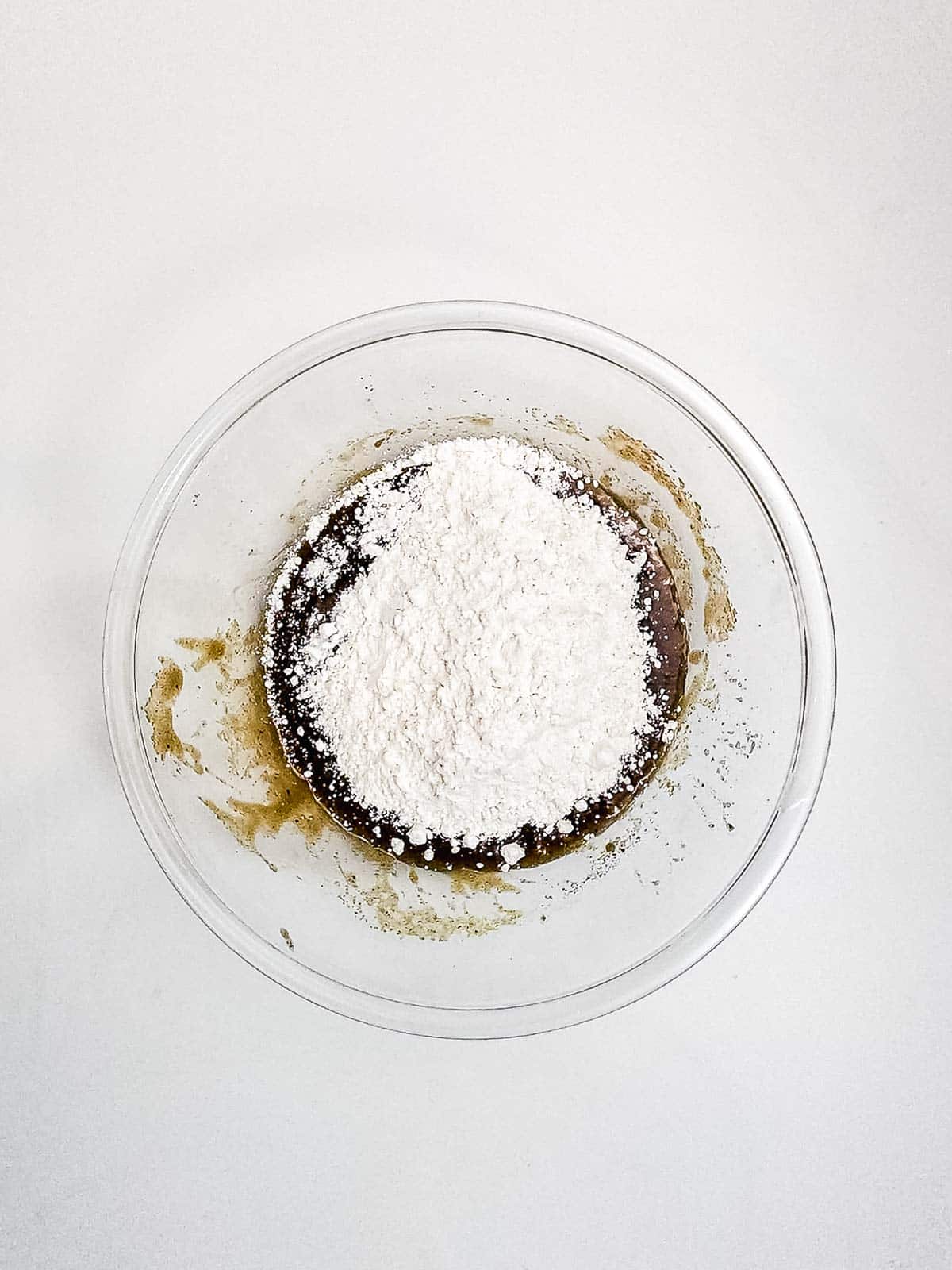 A glass bowl with brown batter and a pile of white flour on top, set on a white surface&mdash;perfect for making Chocolate Chunk Cookies or Air Fryer Cookies.