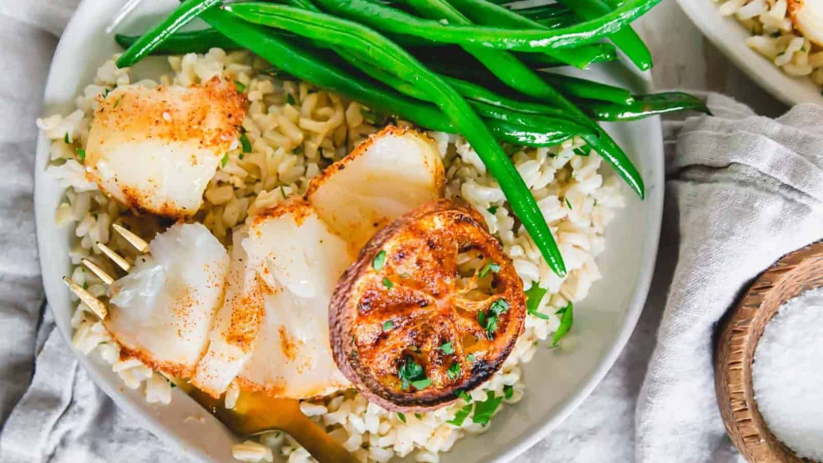 Air fryer cod on a plate with green beans and rice.