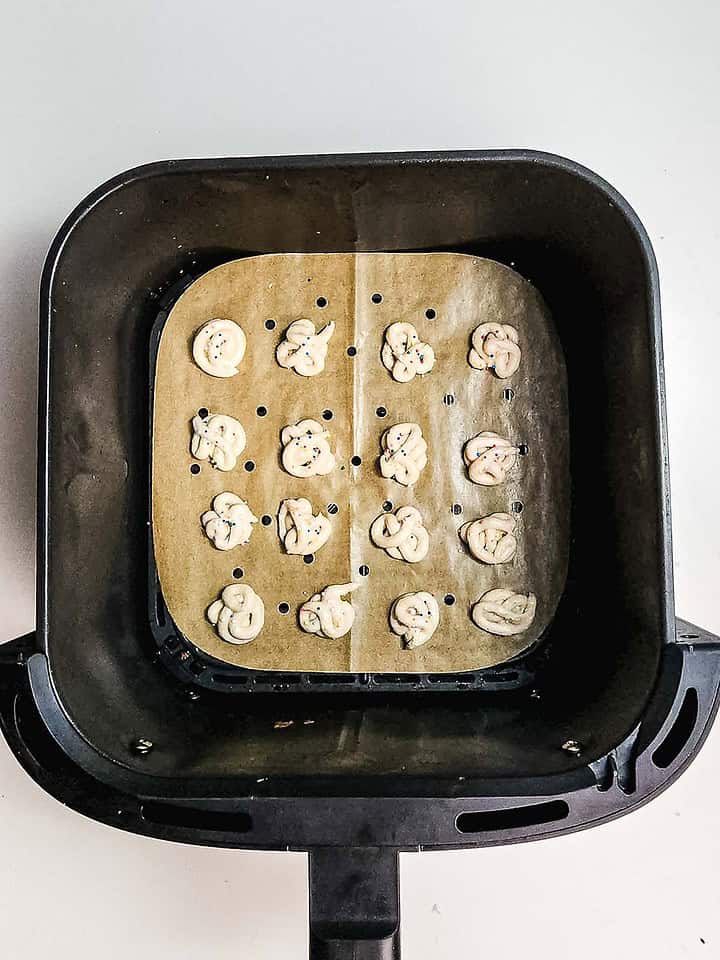 Small pretzel-shaped dough pieces on parchment paper inside an air fryer basket, ready to be cooked—try this easy air fryer recipe for a tasty twist similar to funnel cake bites.