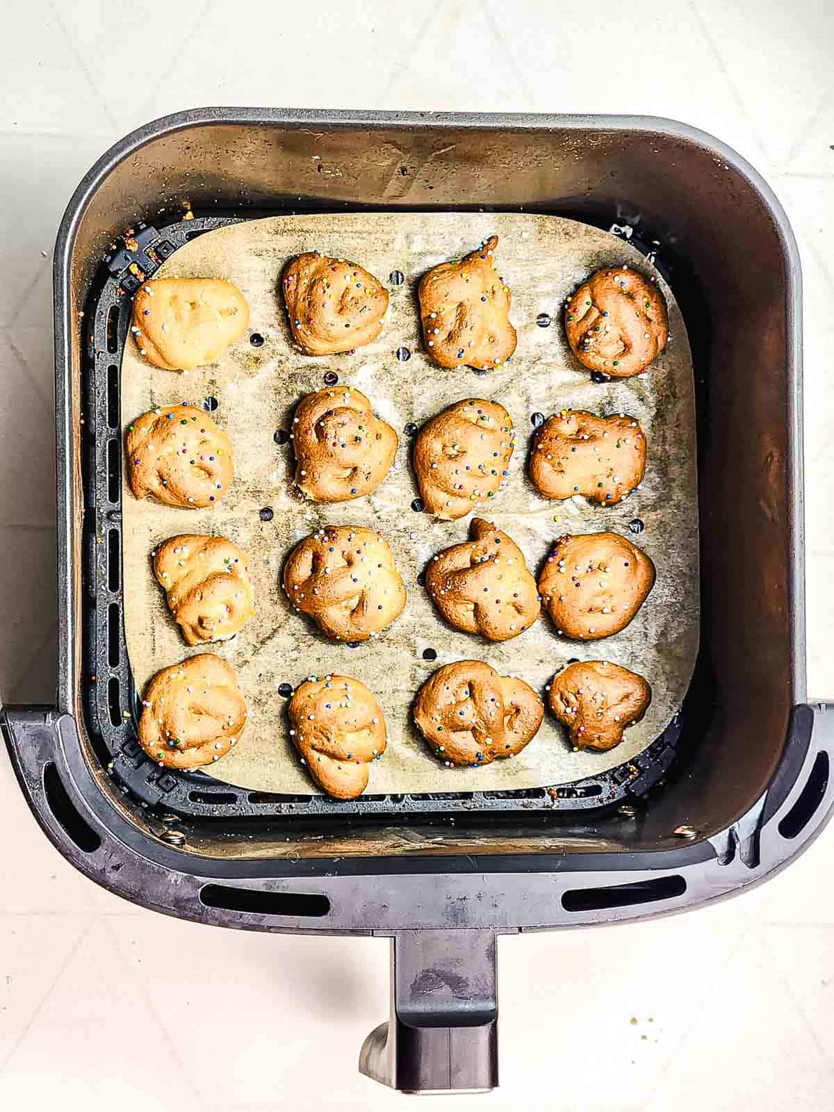 Small pretzel bites sprinkled with seasoning sit on parchment paper in an air fryer basket—try this easy recipe for a fun twist alongside classics like Funnel Cake Bites.