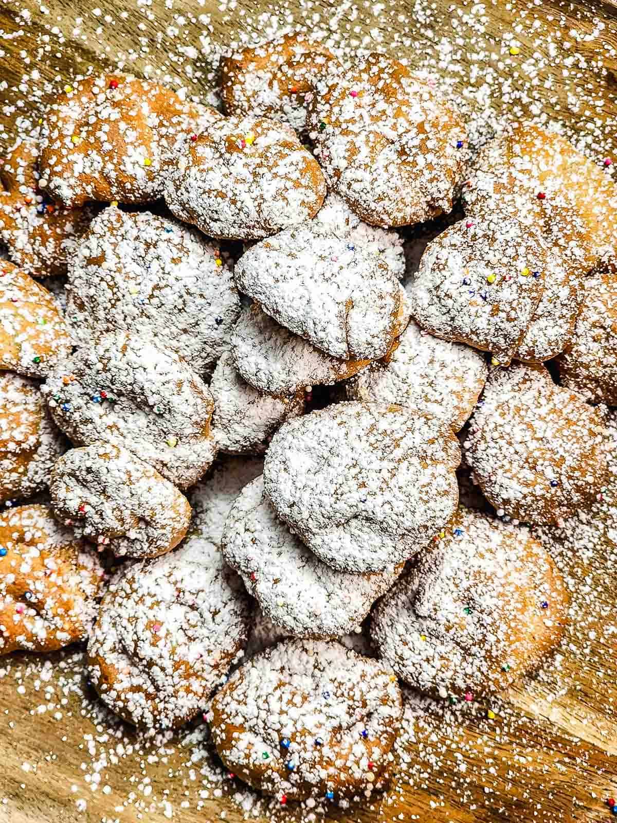 A pile of Funnel Cake Bites dusted with powdered sugar and colorful sprinkles on a wooden surface—an irresistible treat perfect for any recipe collection.