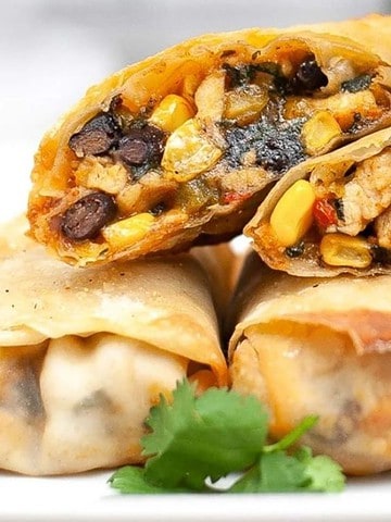 Five crispy egg rolls stuffed with black beans, corn, and vegetables, arranged on a white plate with cilantro.