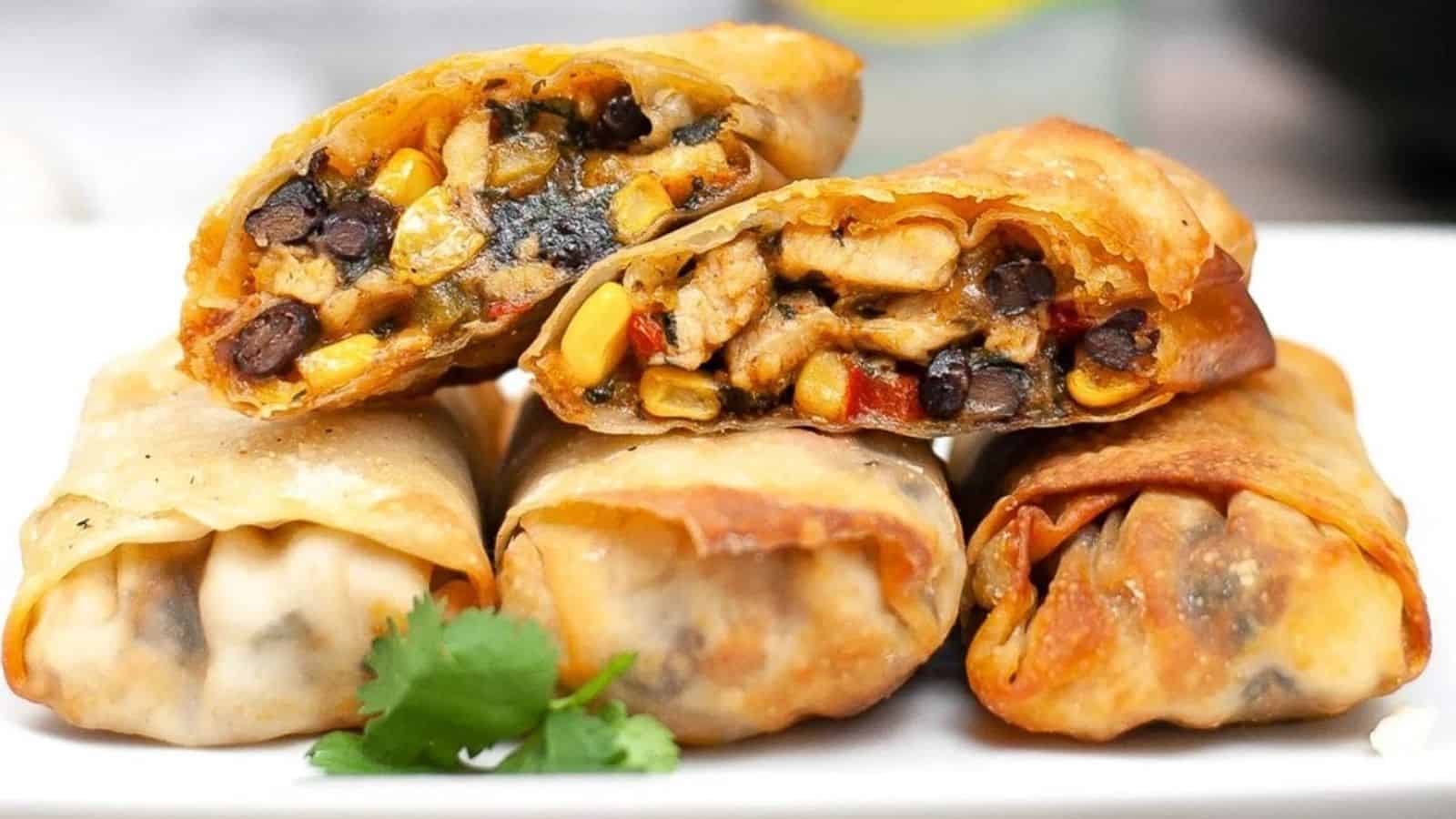 Air fryer southwest egg rolls stacked on plate with the top egg roll cut in half to see the inside chicken filling.